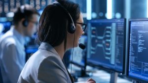 In the System Control Center Woman working in a Technical Support Team Gives Instructions with the Help of the Headsets. Possible Air Traffic/ Power Plant/ Security Room Theme.